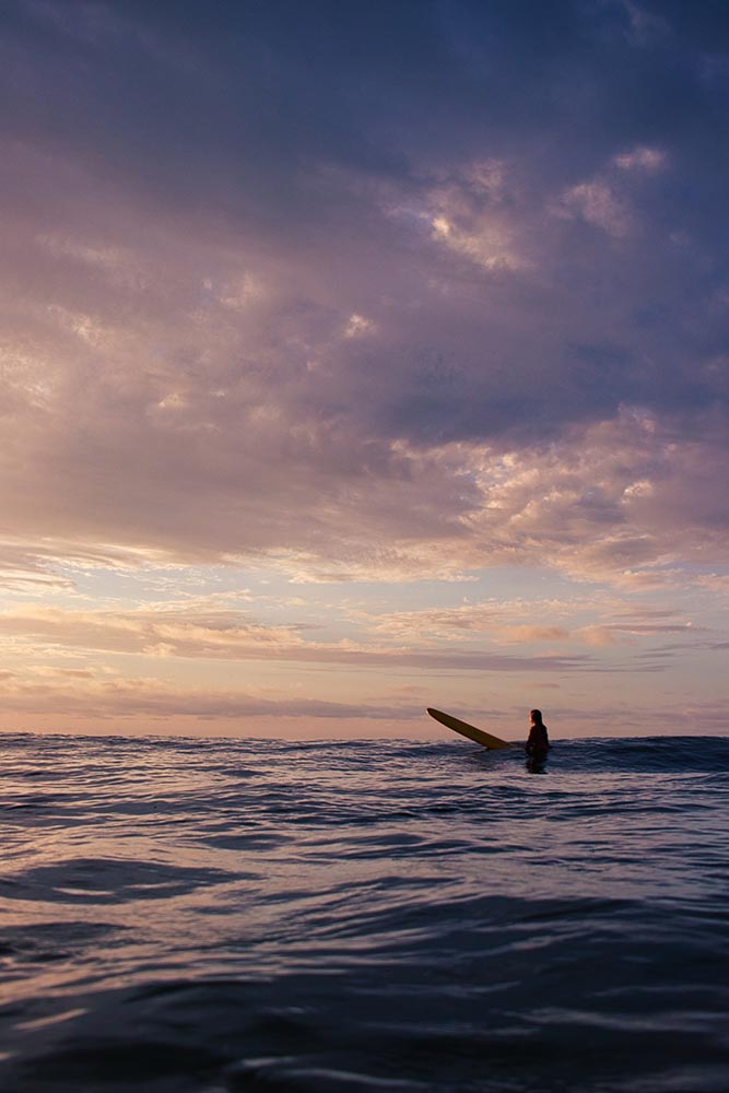 Surfer sitting on longboard at sunrise